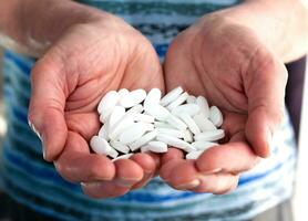 antiguo hombre sostiene muchos blanco pastillas en su manos. medicina concepto. cuidando para el salud de el anciano. de cerca. foto