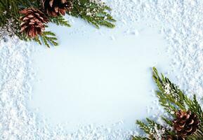 Christmas or winter composition. Frame made of snow, fir branches and fir cones on blue background. New year greeting card. Christmas or New Year flatlay. Top view. Copy space. photo