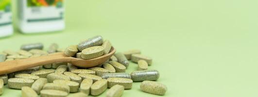 Natural vitamins and supplements in a wooden spoon on a green background. Banner. Close-up. Copy space. Selective focus. photo