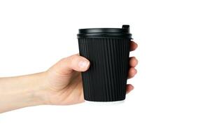 A woman's hand holds a disposable corrugated black paper cup with coffee isolated on a white background. Close-up. Selective focus. photo