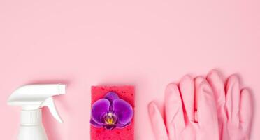 Spring cleaning concept. Detergent, orchid flower, kitchen sponge and rubber gloves on a pink background. Flatlay. Banner. Copy space. Top view. photo