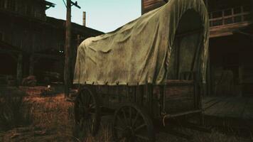 A rustic covered wagon parked next to a charming building in a scenic field photo