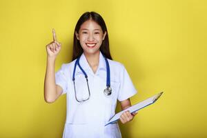 Portrait of a beautiful young woman in a yellow background,  Friendly beautiful woman wearing a doctor's uniform and pointing while wearing a stethoscope. photo