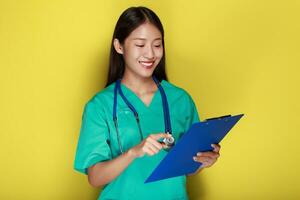 Beautiful young woman makes a thoughtful expression while wearing a doctor's uniform standing in front of a yellow background. photo