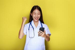 Portrait of a beautiful young woman in a yellow background, Asian woman poses with a cell phone while wearing a doctor's uniform and a stethoscope. photo