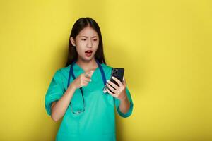 Portrait of a beautiful young woman in a yellow background, Asian woman poses with a cell phone while wearing a doctor's uniform and a stethoscope. photo