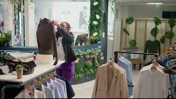 Woman changing clothes on mannequin after restocking elegant high end fashion boutique. Happy worker changing old season clothing with stylish garments from new collection in clothing shop video