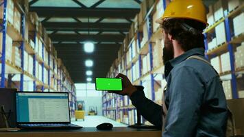 Warehouse manager looks at greenscreen on smartphone display, working on parcel shipment and delivery in industrial depot. Quality control advisor using blank copyspace mockup screen. video