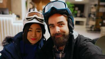 POV of couple answering videocall chat on smartphone, discussing with friends about winter adventure at alpine luxury hotel. Man and woman talking on online conference, mountain resort. Handheld shot. photo