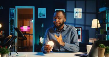 Content creator in dimly lit apartment studio uses camera to film smart light bulb review for online streaming platforms. Online star hosts internet show, unboxing IoT home automation product photo