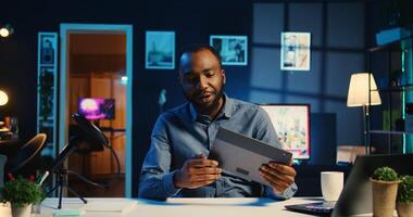 BIPOC content creator filming technology review of newly launched tablet, unpacking it and presenting specifications to audience. Internet star showing digital device to viewers photo
