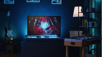 Panning shot of empty home studio illuminated with neon lights used for internet video production. Living room filled with content creation equipment, TV animations running in background photo