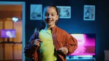 Joyful kid dancing in dimly lit home studio interior, producing content for online channel with smartphone on tripod. Smiling child doing viral dance choreography in living room photo