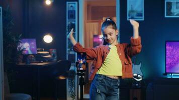 Kid doing viral dance choreography in living room with 3D rendered animations on computer screens in background. Child dancing in neon lit home studio interior, producing content with cellphone photo