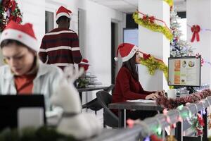 Focused employees researching key data for company project during Christmas holiday season. Multiethnical business team solving tasks in festive decorated office before approaching deadline photo