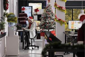 Business team working in busy festive decorated office during Christmas holiday season. Hardworking employees solving various company project tasks in xmas ornate workspace photo