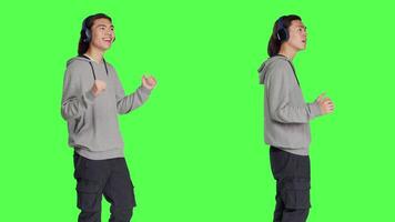 Person listening to tunes and dancing in studio with audio headset, having fun with music and groovy dance moves. Joyful man feeling optimistic and confident, greenscreen backdrop. video