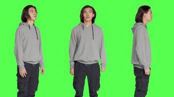 Asian friendly model standing in studio and posing with confidence, smiling against isolated greenscreen background. Young adult acting optimistic and relaxed in casual jeans. video