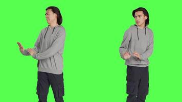 Male model pretending to push something aside, expressing rejection or refusal in studio. Young man mimicking dismissal over isolated greenscreen background, stop symbol. video