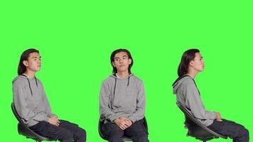 Young man checking wristwatch and waiting in studio, acting impatient while sitting on chair over greenscreen. Male model looking at time on camera, optimistic person with watch. video