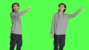 Model indicating left or right directions in studio, pointing to both sides and recommending another path. Asian young guy advising people to go this way using index fingers, greenscreen. video