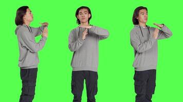 Person does timeout gesture with hands, asking for a break or pause against greenscreen in studio. Asian man showing disapproval and negative emotions on camera, stop gesture. video