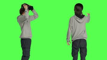 ung kille åtnjuter virtuell verklighet enhet i studio med grönskärm bakgrund, använder sig av interaktiv syn på glasögon. modern person har roligt med artificiell intelligens vr headset. video