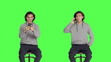 Asian adult texting and answering call on greenscreen background, sending messages on social media using smartphone app. Young man sitting on chair, calling friends and messaging. video