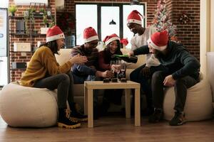 Cheerful employees pouring alcohol beverage into glasses to celebrate christmas season. Happy colleagues gathering together for xmas eve holiday dinner in decorated office photo