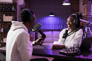 Online show host enjoying banter with african american comediant sharing favourite jokes during comedy focused podcast. Interviewer broadcasting live from living room studio adorn with rgb lights photo