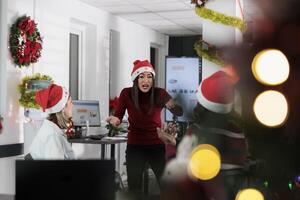 Manager angry at employees, frustrated by weak company performance after checking year end analytics during Christmas season. Management executive yelling at staff members in festive decorated office photo