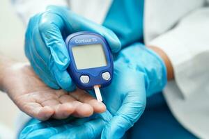 Asian doctor using digital glucose meter for check sample blood sugar level to treatment diabetes. photo