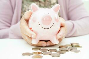 Retired elderly woman counting coins money with piggy bank and worry about monthly expenses and treatment fee payment. photo