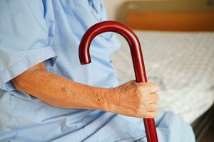 Asian elderly disability woman patient holding walking stick in wrinkled hand at hospital. photo