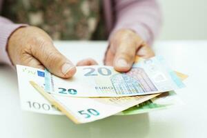 Retired elderly woman holding Euro banknotes money and worry about monthly expenses and treatment fee payment. photo