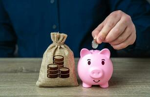 A man puts coins in a piggy bank. Accumulating money. Savings and investments. Bank deposit. Raise funds for your dream. Reduce costs. Save for retirement. Collection of donations. photo