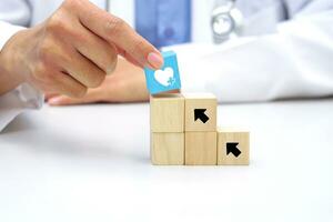 Hand holding a wooden block cube the top one with heart icon symbol. Medical and health concept. photo