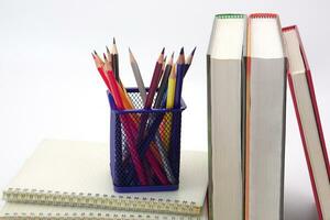 Crayon or colored pencils in box laying on a stack of books, white background. Knowledge and education concept. photo