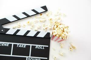 Focus of popcorn and blur clapperboard or movie slate black color on white background. Cinema industry, video production and film concept. photo