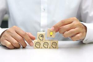 Wooden blocks with head human icon arranged in stair shape, hand hold wooden cube block with light bulb icon symbol. Brainstorming or innovative idea concept. photo