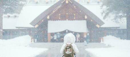 mujer turista visitando en sapporo, viajero en suéter mirando Hokkaido santuario con nieve en invierno estación. punto de referencia y popular para atracciones en Hokkaidō, Japón. viaje y vacaciones concepto foto