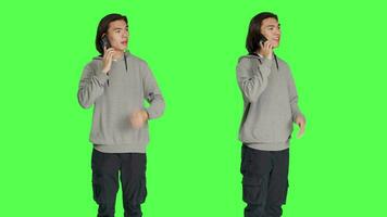 Modern person chatting on phone call against greenscreen backdrop, using smartphone line to talk to his friends in studio. Young adult answering call to have remote conversation. video