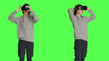 ung vuxen åtnjuter virtuell verklighet tech i studio med grönskärm bakgrund, använder sig av interaktiv 3d syn på headset. modern kille har roligt med artificiell intelligens vr glasögon. video