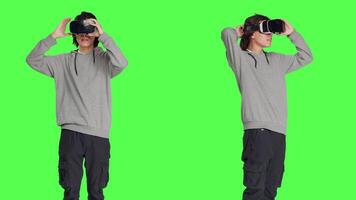 Young adult enjoys virtual reality tech in studio with greenscreen backdrop, using interactive 3d vision on headset. Modern guy having fun with artificial intelligence vr glasses. video