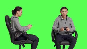 Asian gamer playing video games over greenscreen background, using controller and enjoying gameplay with friends online. Young person having fun with rpg competition on console.