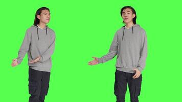 Male model creating advertisement showing something to left or right sides in studio, pointing at thing over greenscreen background. Young guy advertising slogan for marketing industry. video