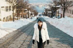 Woman tourist Visiting in Hakodate, Traveler in Sweater sightseeing Hachiman Zaka Slope with Snow in winter. landmark and popular for attractions in Hokkaido, Japan. Travel and Vacation concept photo