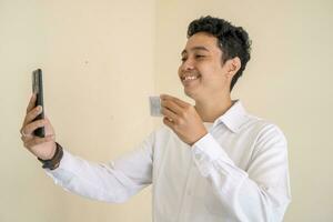Indonesian man wear white clothes with selfie with id card looking to camera photo