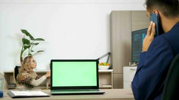 laptop met een groen scherm Aan de tafel in de leven kamer. een Mens is pratend Aan de mobiele telefoon terwijl een vrouw Toneelstukken video spellen in de achtergrond Aan de troosten. dolly schuif 4k beeldmateriaal