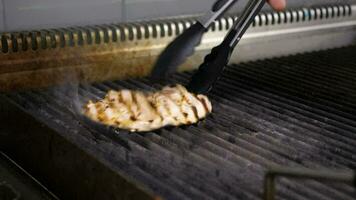 Turning from one to another a piece of grilled chicken meat on restaurant grill video